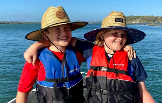 Deux enfants se tenant dans les bras, portant des gilets de sauvetage et des chapeaux de paille.