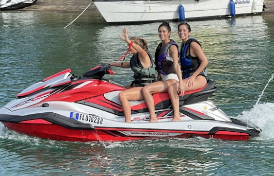 Tres niñas, todas con chalecos salvavidas, sonriendo mientras viajan con seguridad en una moto acuática.